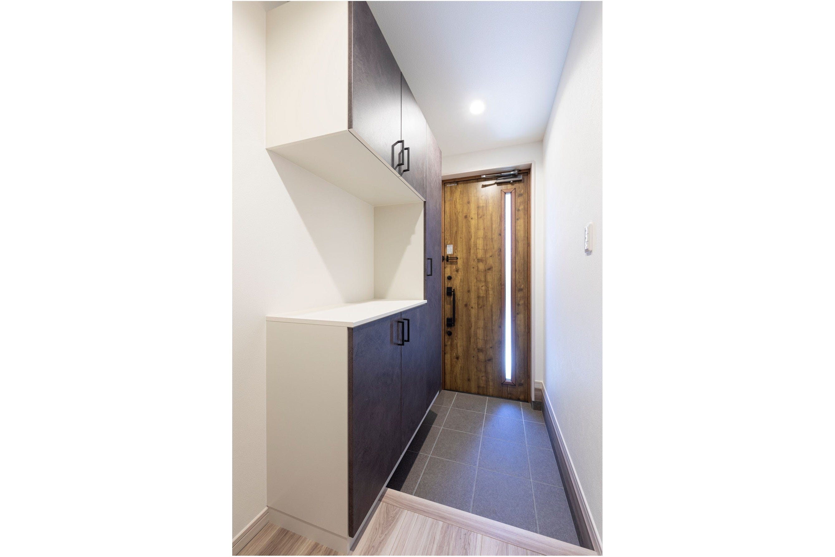 木目調の玄関ドアが温かみを感じさせるエントランス。
シューズボックスにはグレーとホワイトのツートンカラーを採用し、シンプルながらも洗練された印象に。
限られたスペースの中でも、収納力とデザイン性を両立させた設計です