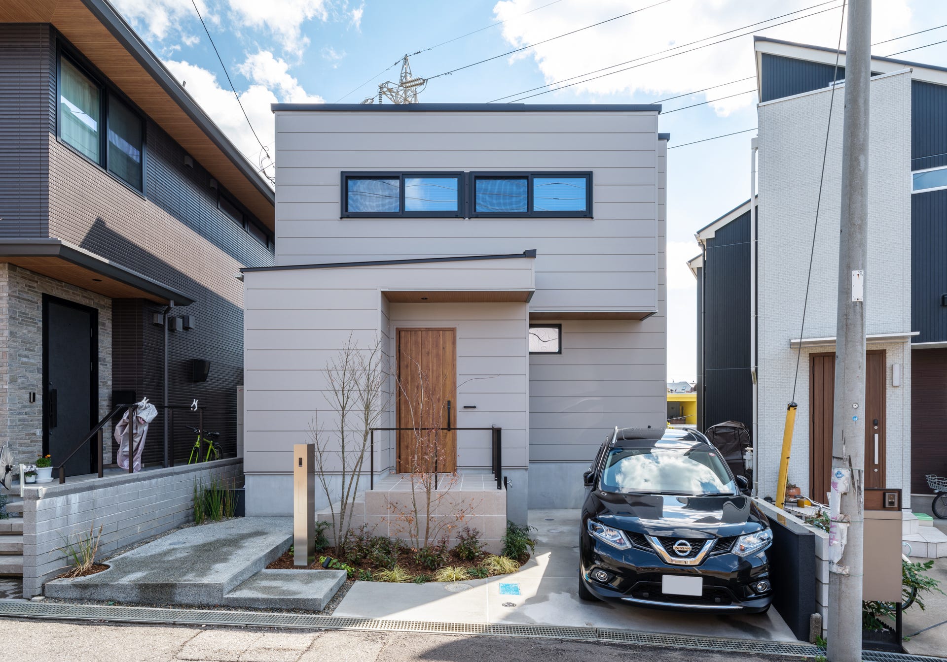 建築工房　櫓　陰影を纏う家 (高台と緑地が隣接する土地に眺望の良さを活かす建物計画をしました。
玄関側外観デザインは外部からの視線を遮るクローズドな設計としつつ、高台側はLDKに大きな掃き出しの窓と吹き抜けを設けることで、光と風を取り込みます。
プライバシーを守りながら、LDKのどこにいても空や緑を眺める事が出来ます。掃き出し窓の上部には木目の下がり天井で造作した間接照明をレイアウトし、空間に奥行きを与える演出をしました。)