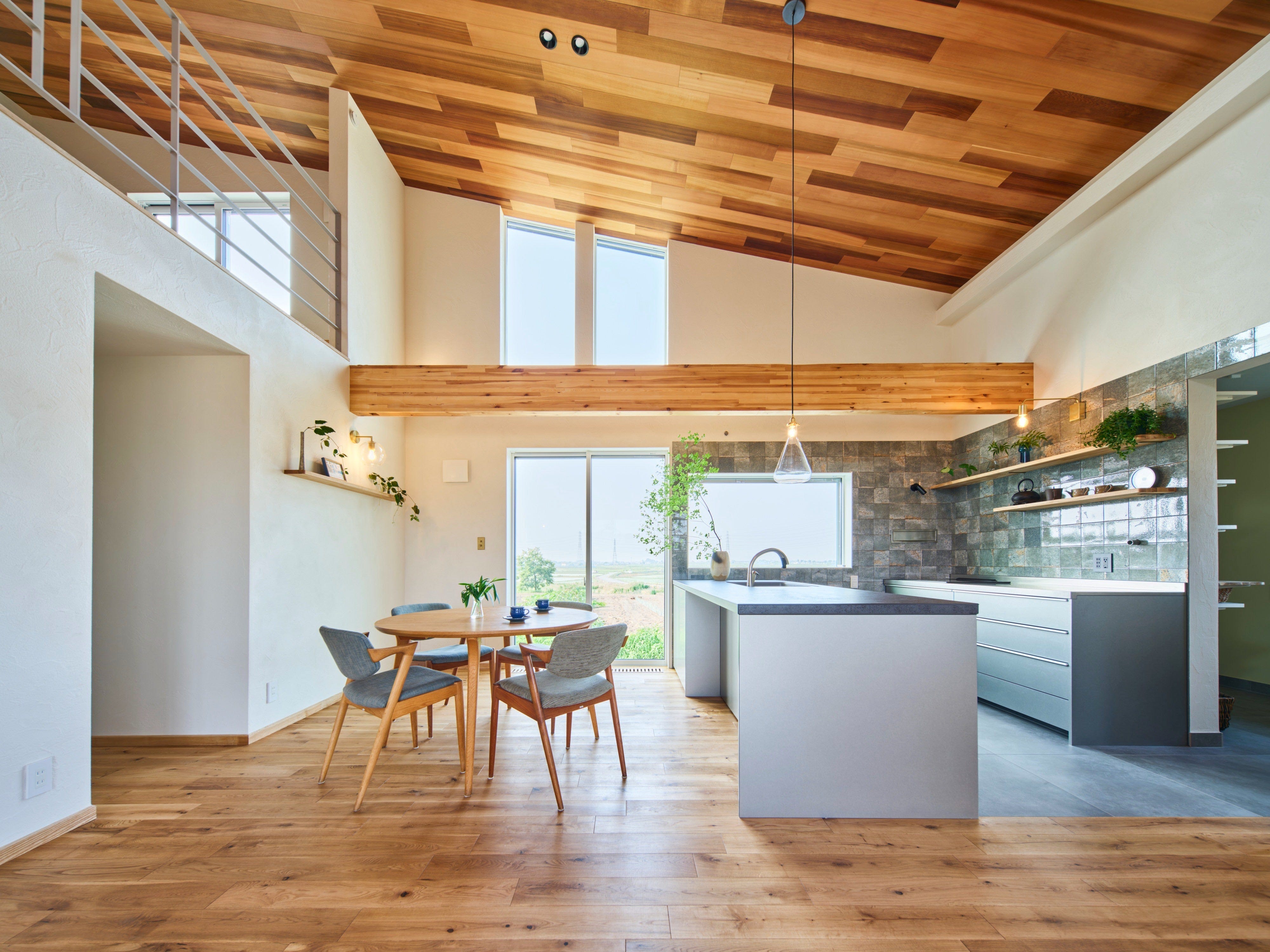 目の前に広がる田園風景を存分に楽しめるよう設計しました。 開放感のある大きな吹抜けの板貼りと梁あらわしで木の温もりが心地よく、家族や仲間とくつろぐ時間を明るく豊かにしてくれる空間です。