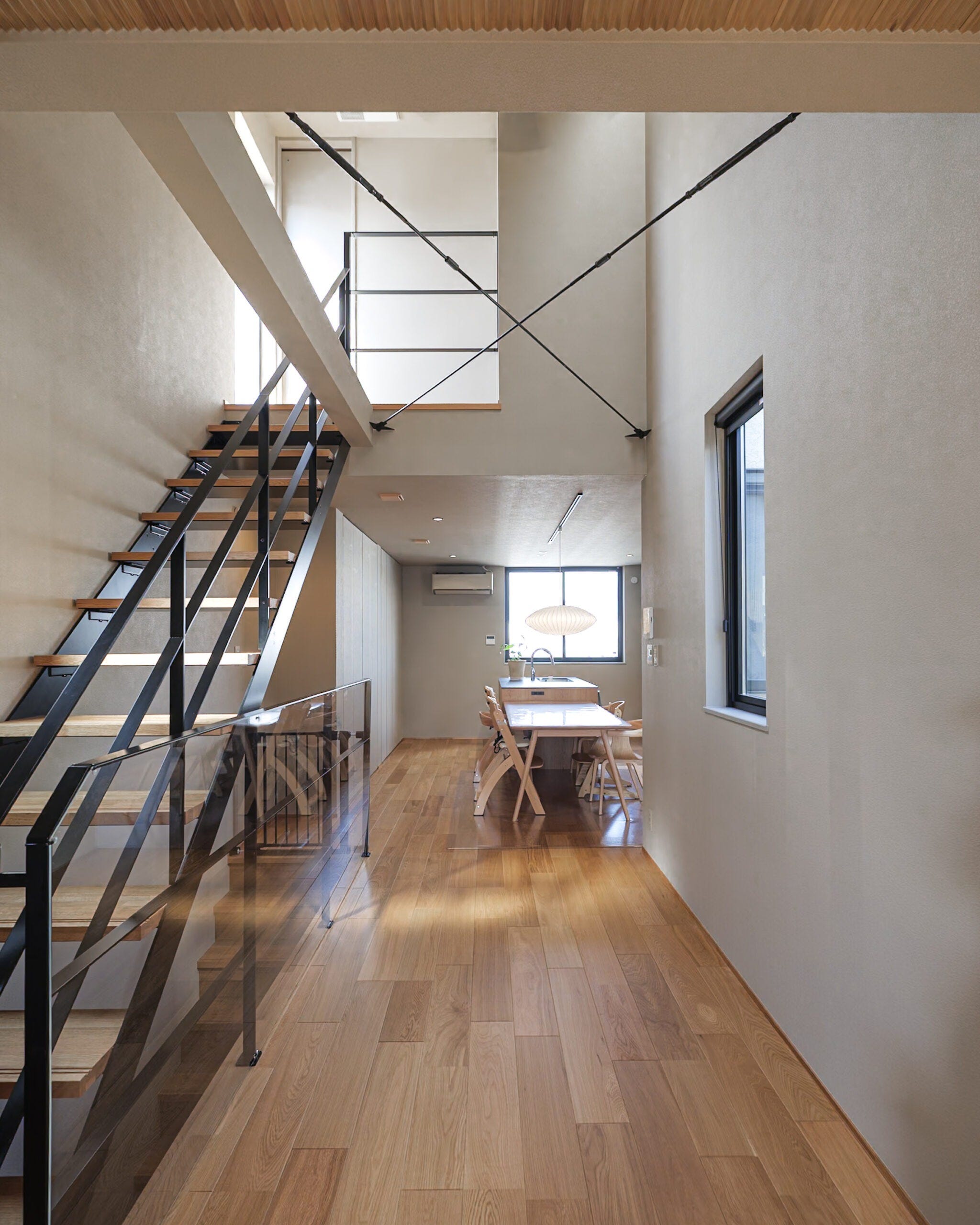 吹き抜けがもたらす開放感と、グレージュのやわらかな色合いが心地よく調和した空間。スチール階段のシャープなラインがアクセントとなり、洗練された雰囲気の中に温もりある木の質感が際立ちます。光が奥まで届く設計で、家のどこにいても心地よさを感じられる住まいです。