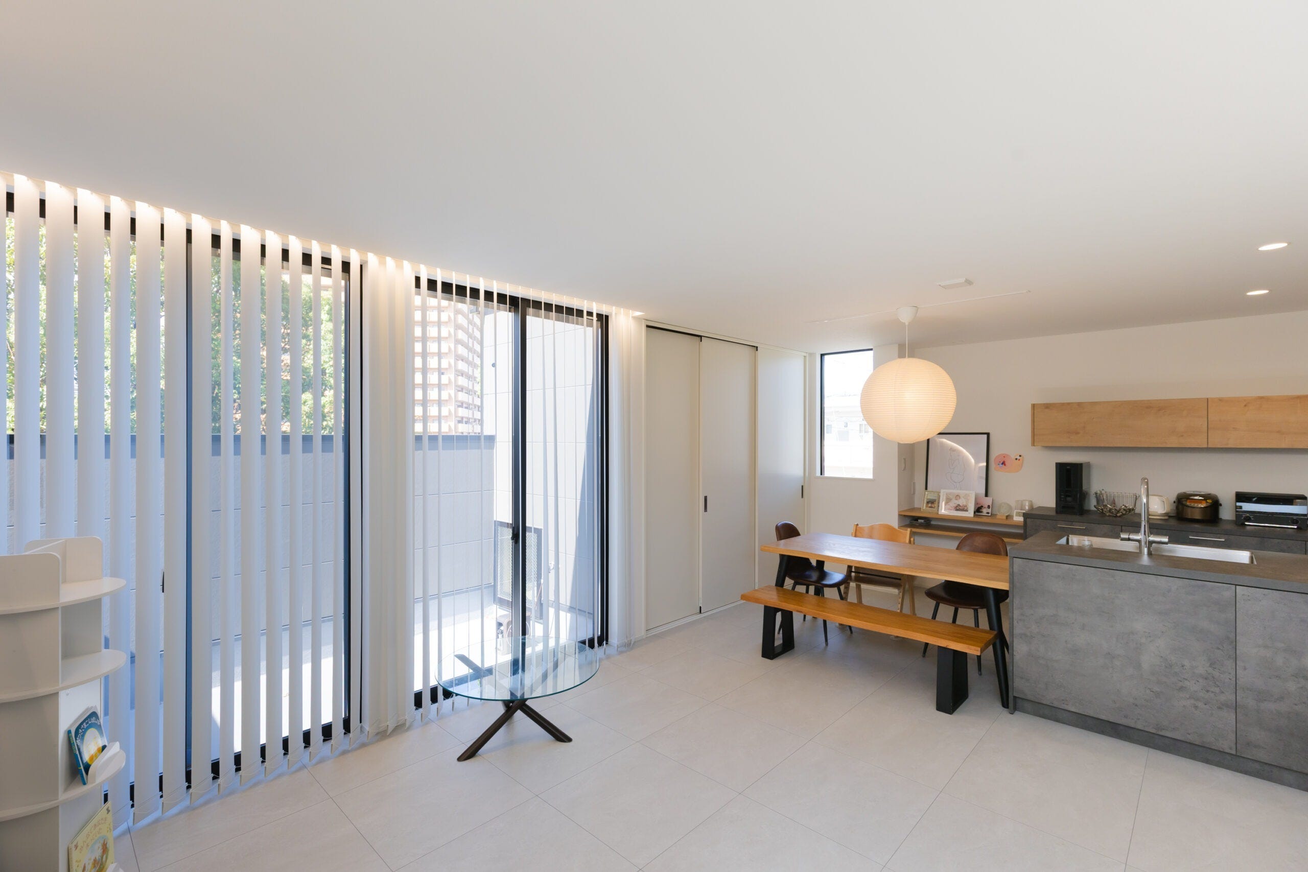 大きな窓から自然光がたっぷりと注ぐ、明るく開放的なリビング・ダイニング。カーテンレスでも心地よく過ごせるよう、外からの視線を考慮した設計。グレーとナチュラルウッドを基調としたインテリアが、落ち着きのある上質な空間を演出。